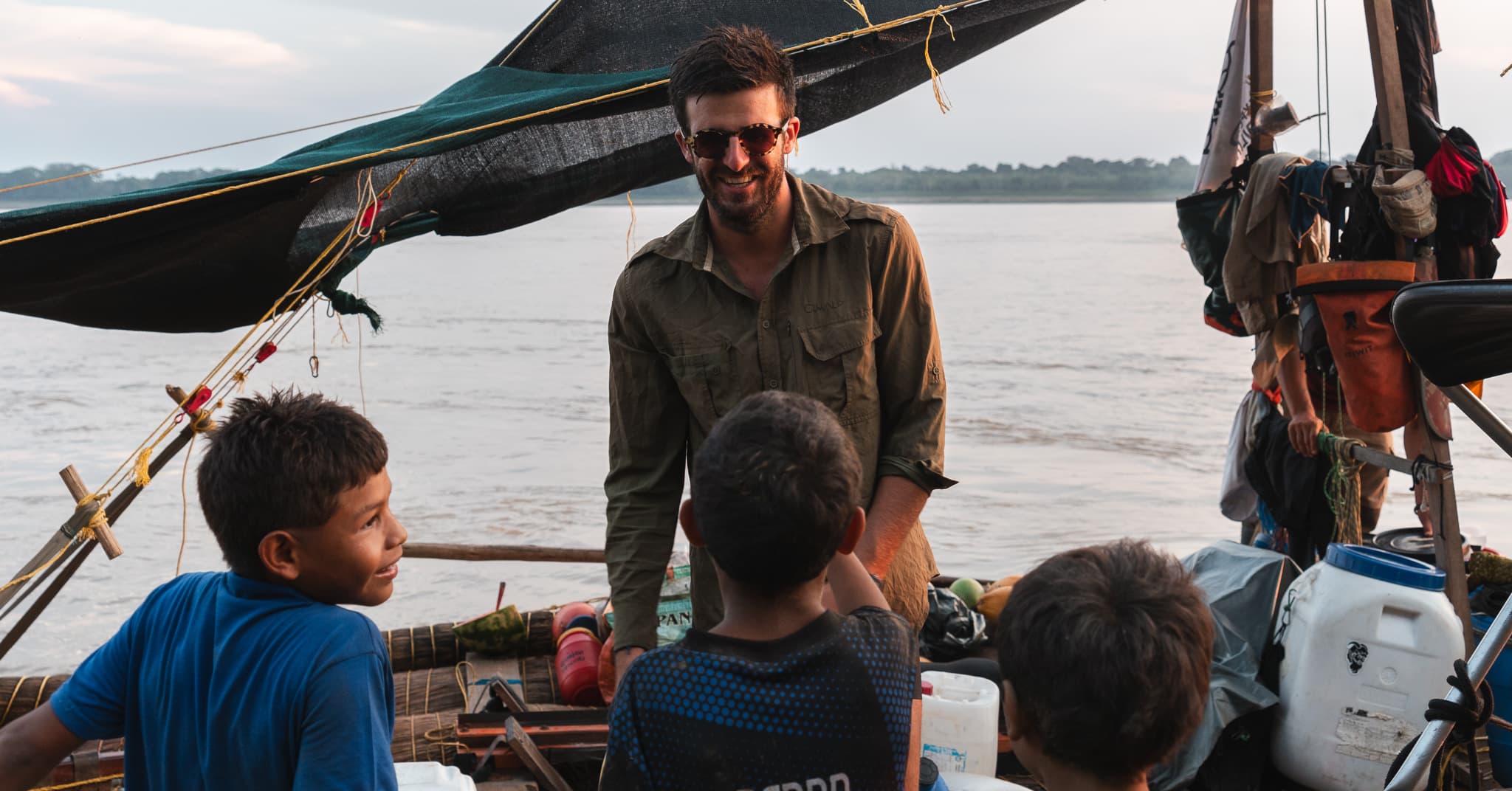 Au crépuscule, un membre de l'équipage échange avec trois enfants montés à bord de la balsa