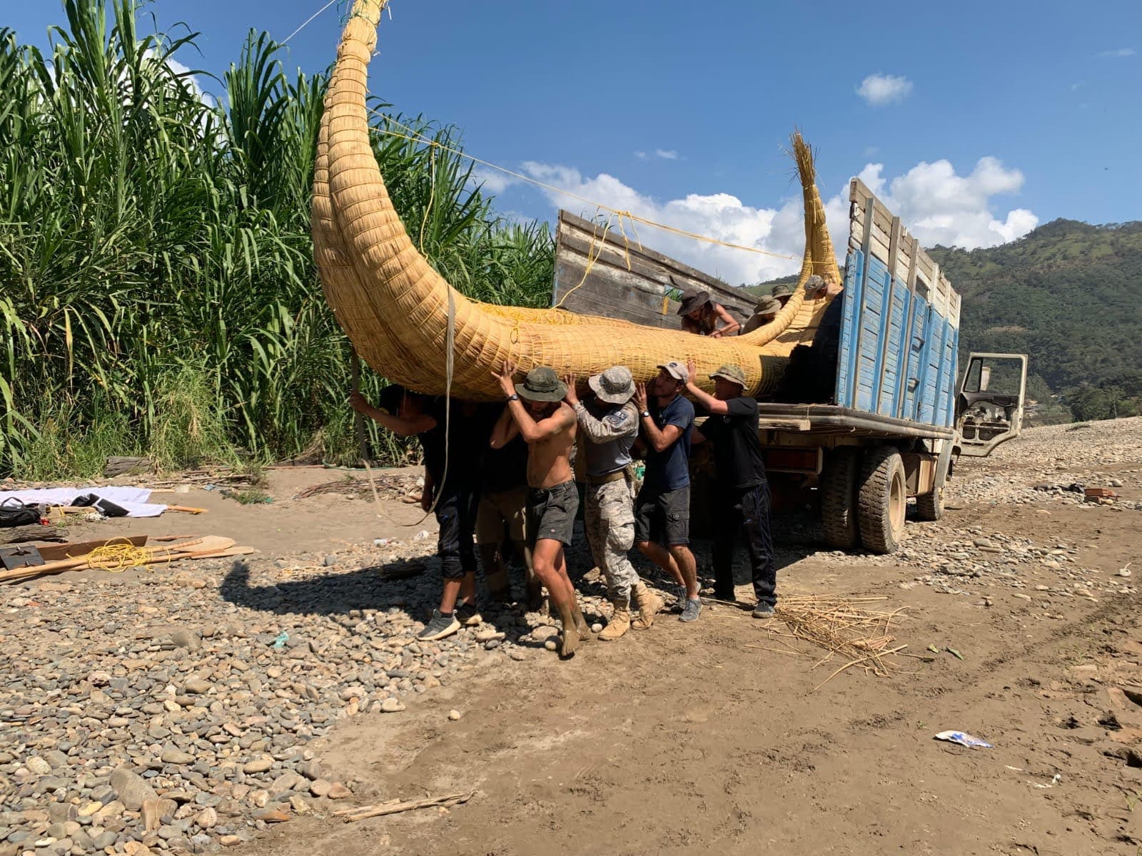 L'équipage et des militaires portent à l'épaule une coque de totora déchargée d'un camion, au bord du fleuve